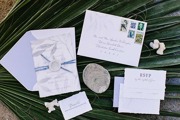 Romantic Wedding Invitation, gray watercolor leaf pattern on vellum overlay, vintage stamps, torn edges, palm fronds and sea shells in the background